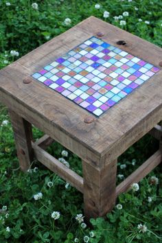 a small wooden table with a mosaic tile top on it's legs in the grass