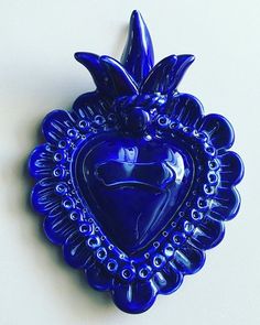 a blue heart shaped brooch sitting on top of a white table next to a wall