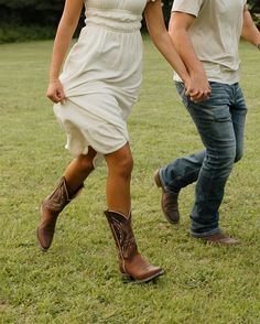 a man and woman are walking in the grass holding hands with each other while wearing cowboy boots