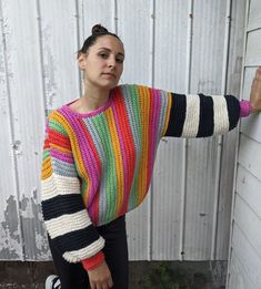 a woman leaning against a wall wearing a multicolored sweater