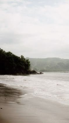 an empty beach with waves coming in to shore and trees on the other side,