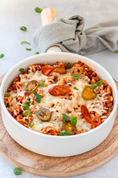 a white casserole dish with tomatoes, cheese and other toppings on a wooden board