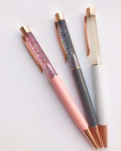 three different colored pens sitting next to each other on a white surface with gold trim