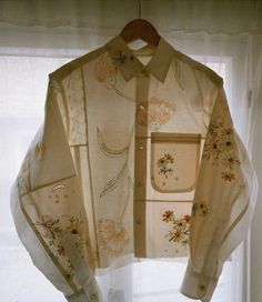 an embroidered shirt hanging on a window sill in front of a white sheer curtain