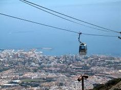 two people ride the gondola on top of a mountain overlooking cityscape