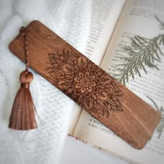 a wooden bookmark with a tassel on top of an open book next to a plant