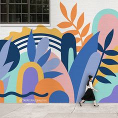 a woman walking past a colorful mural on the side of a building