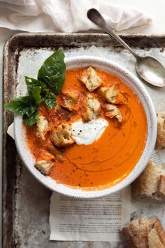 a bowl of tomato soup with bread on the side