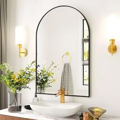 a white sink sitting under a large mirror next to a vase with flowers in it