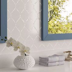 a white vase with flowers in it sitting on a counter next to two blue framed mirrors