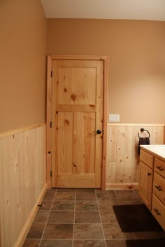 a wooden door in a bathroom next to a sink and counter with the word happiness written on it