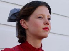 a woman wearing a red sweater and a blue bow on her head looking off to the side