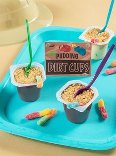 three cups filled with cereal and candy on a blue tray next to a sign that says pudding dirt cups