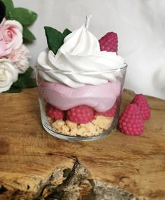 a dessert with raspberries and whipped cream in a small glass dish on a wooden table