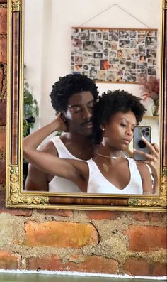 a man and woman taking a selfie in front of a brick wall with a gold framed mirror