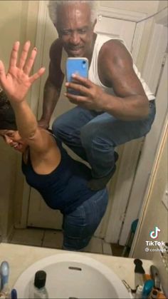 a man taking a selfie in front of a bathroom mirror with his hands up