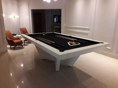 a pool table in the middle of a room with two chairs around it and lights on