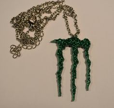 a green monster necklace on a white table next to it's chain and pendant