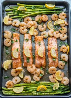 grilled salmon and shrimp with asparagus on a baking sheet topped with lemon wedges