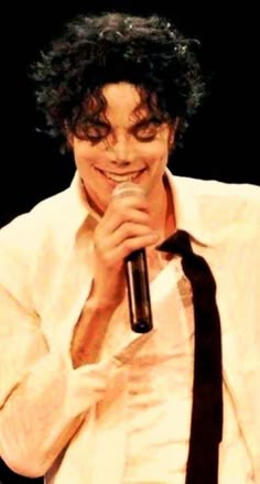 a man holding a microphone in his right hand and smiling at the camera while wearing a white shirt and black tie