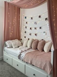 a bed with lots of pillows on top of it and string lights hanging from the ceiling