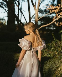 a woman in a white dress is walking through the grass with her back to the camera