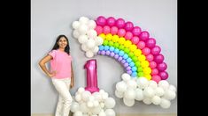 a woman standing in front of a balloon arch with the number one on it and balloons all around her