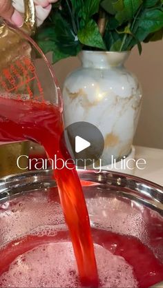 a person pouring red liquid into a metal bowl with flowers in the background and text reading cranberry juice