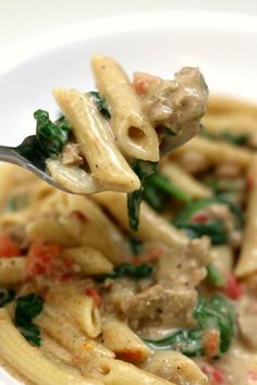 a spoon full of pasta with meat and spinach on it is being held up