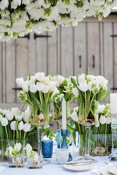 white flowers are in vases on a table with blue and white dishes, candles and napkins