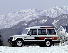 an suv parked in the snow with mountains in the background