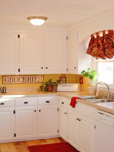 a kitchen with white cabinets and red rugs on the hardwood floored flooring