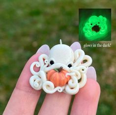 a hand holding a white ring with an octopus on it's face in front of a green background