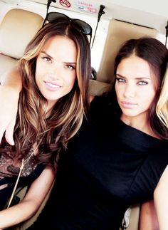 two beautiful young women sitting next to each other on a car seat in front of a mirror