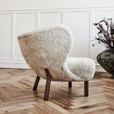 a white chair sitting on top of a wooden floor next to a vase filled with flowers