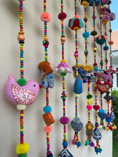 colorful beads hanging from the side of a wall next to a white building with trees in the background