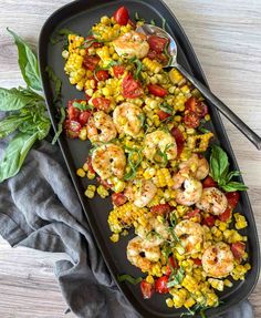 shrimp, corn and tomato salad on a black platter with silverware next to it