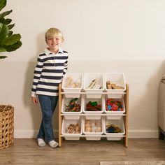 a young boy standing next to a shelf with bins and containers on it in front of a white wall