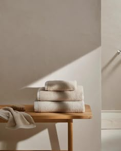 towels are stacked on a wooden table in front of a white wall and floor lamp