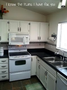 a kitchen with white cabinets and black counter tops is pictured in this image, there are two windows above the sink