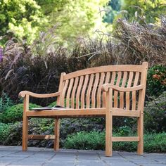 a wooden bench sitting on top of a stone walkway next to bushes and flowers in the background