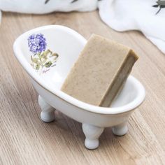 a soap bar sitting in a white bowl on a wooden table next to some flowers