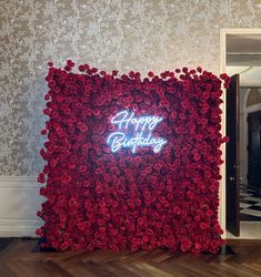 a happy birthday sign made out of red roses on a wall in a room with a black and white checkered floor