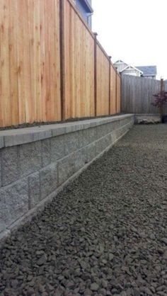 a wooden fence next to a concrete block wall with rocks on the bottom and side