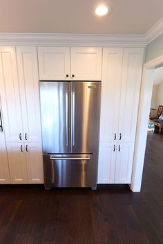 a stainless steel refrigerator in a kitchen with white cabinets and wood flooring on the walls