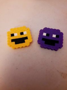 two small legos sitting next to each other on a white surface with one purple and one yellow