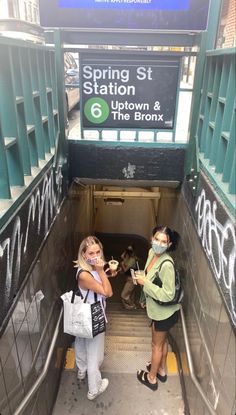 two women standing on an escalator in front of a sign that says spring st station 6 up town and the bronx