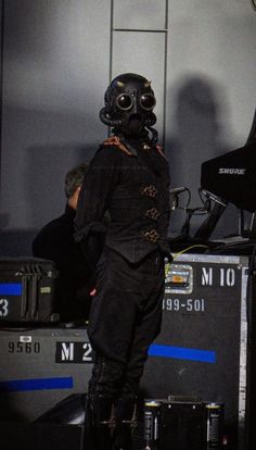 a man in a black suit and gas mask standing next to a piano on stage