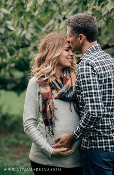 a pregnant couple cuddling under a tree