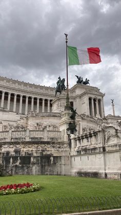 the italian flag is flying in front of an old building with statues and flowers around it